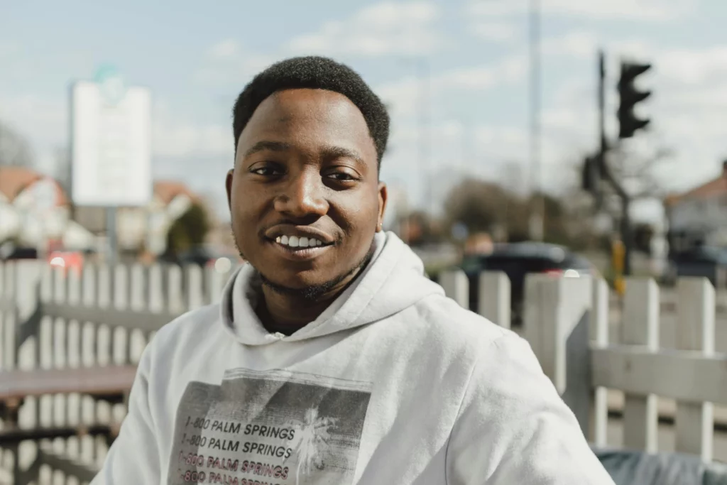 A young man sat on a bench outside smiling at camera