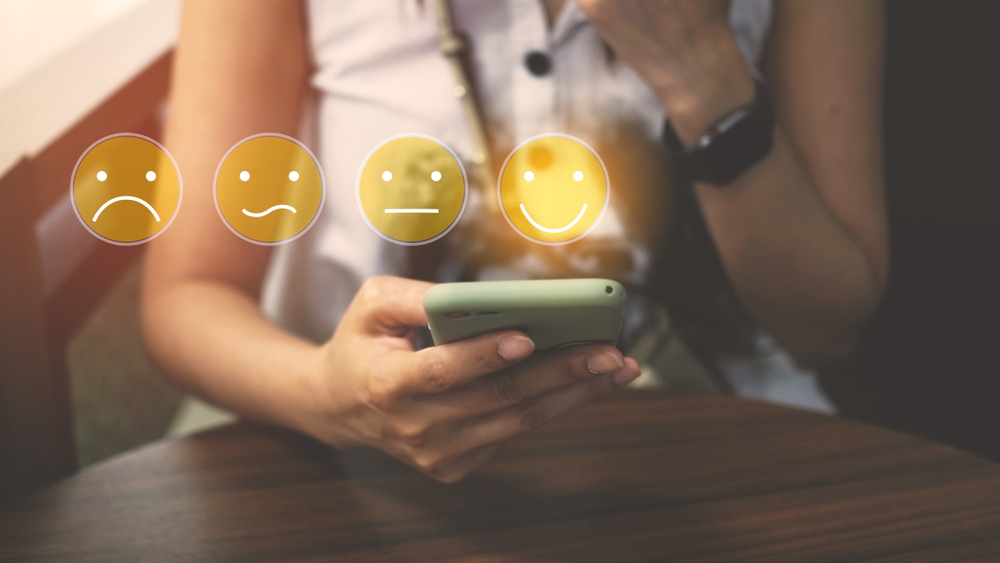 Person giving customer feedback on their phone - emojis for different emotions above